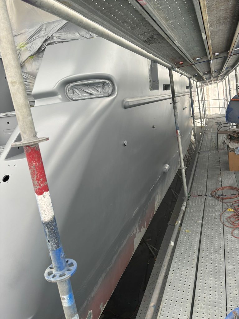 Blue Azimut hull in grey primer inside the scaffold enclosure with openings masked