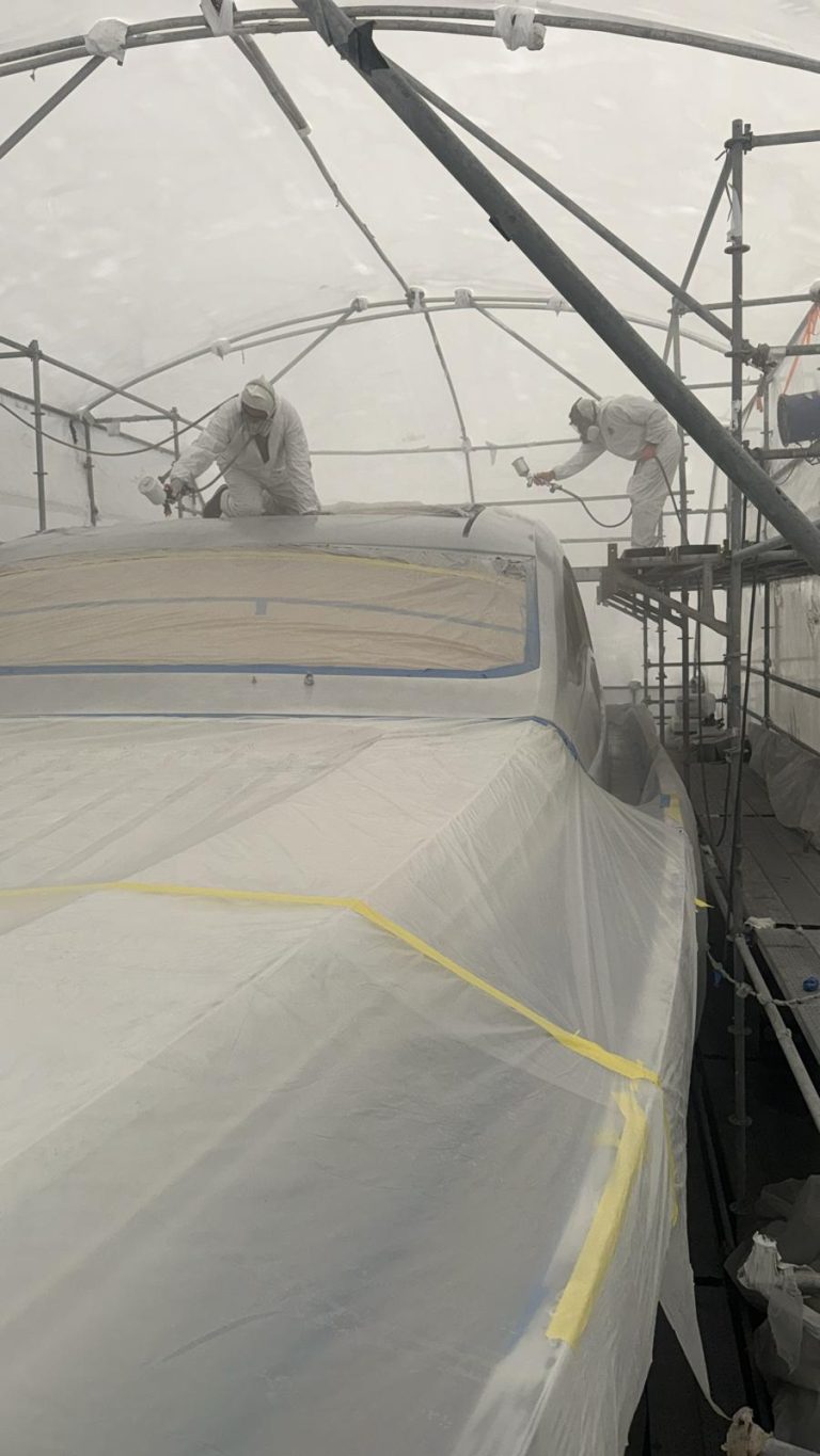 Two painters spraying the Pershing 64 upper exterior inside the enclosure